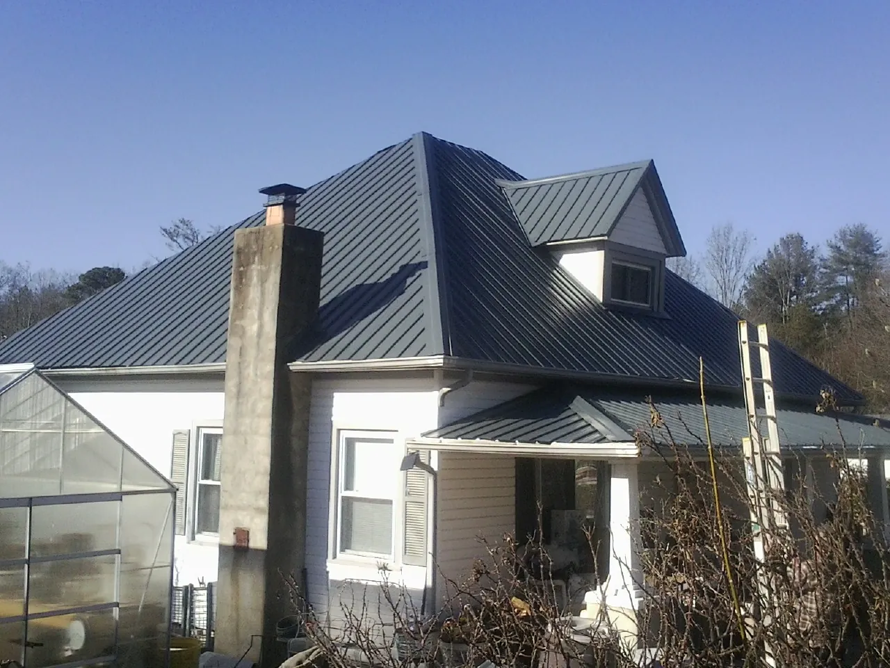 Dark blue standing seam metal roof on a white farmhouse with dormer — Slate & Tile Roof Repair by Roofing Brothers in Wakita