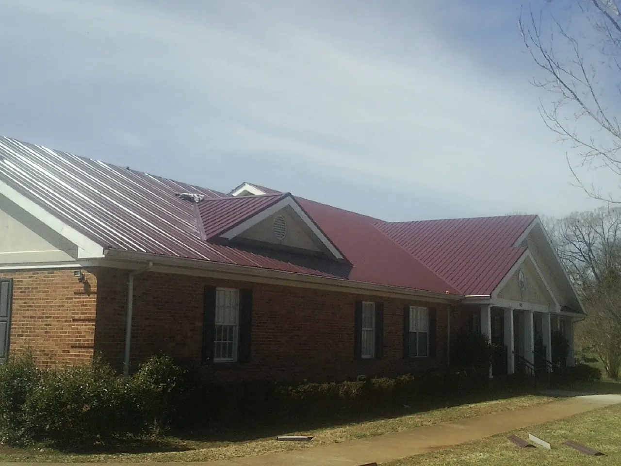 Red metal roof with gabled entries on a long brick building, from a Hail Damage Roof Repair job in Wakita