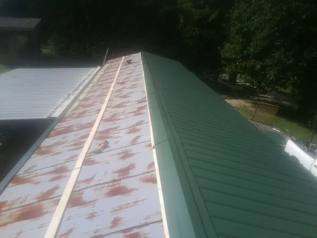 Old rusted panels beside newly installed green metal roofing — Wind Damage Roof Repair by Roofing Brothers in Wakita