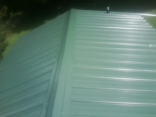 New green metal panels meeting at the ridge of a roof — Flat Roof Repair work by our crew in Wakita