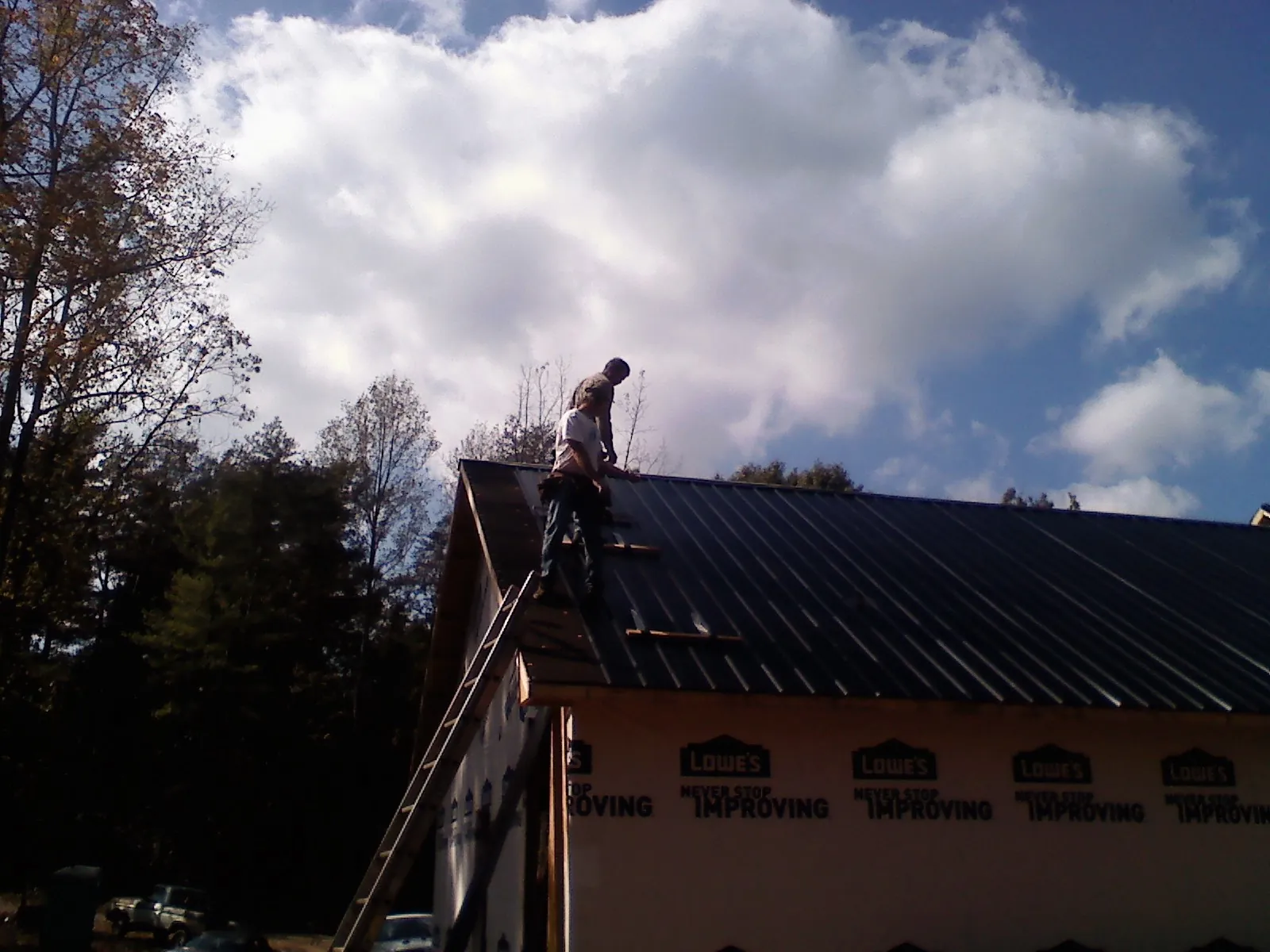 Roofer fastening dark metal panels high against a cloudy sky, from a Roof Inspection job in Wakita