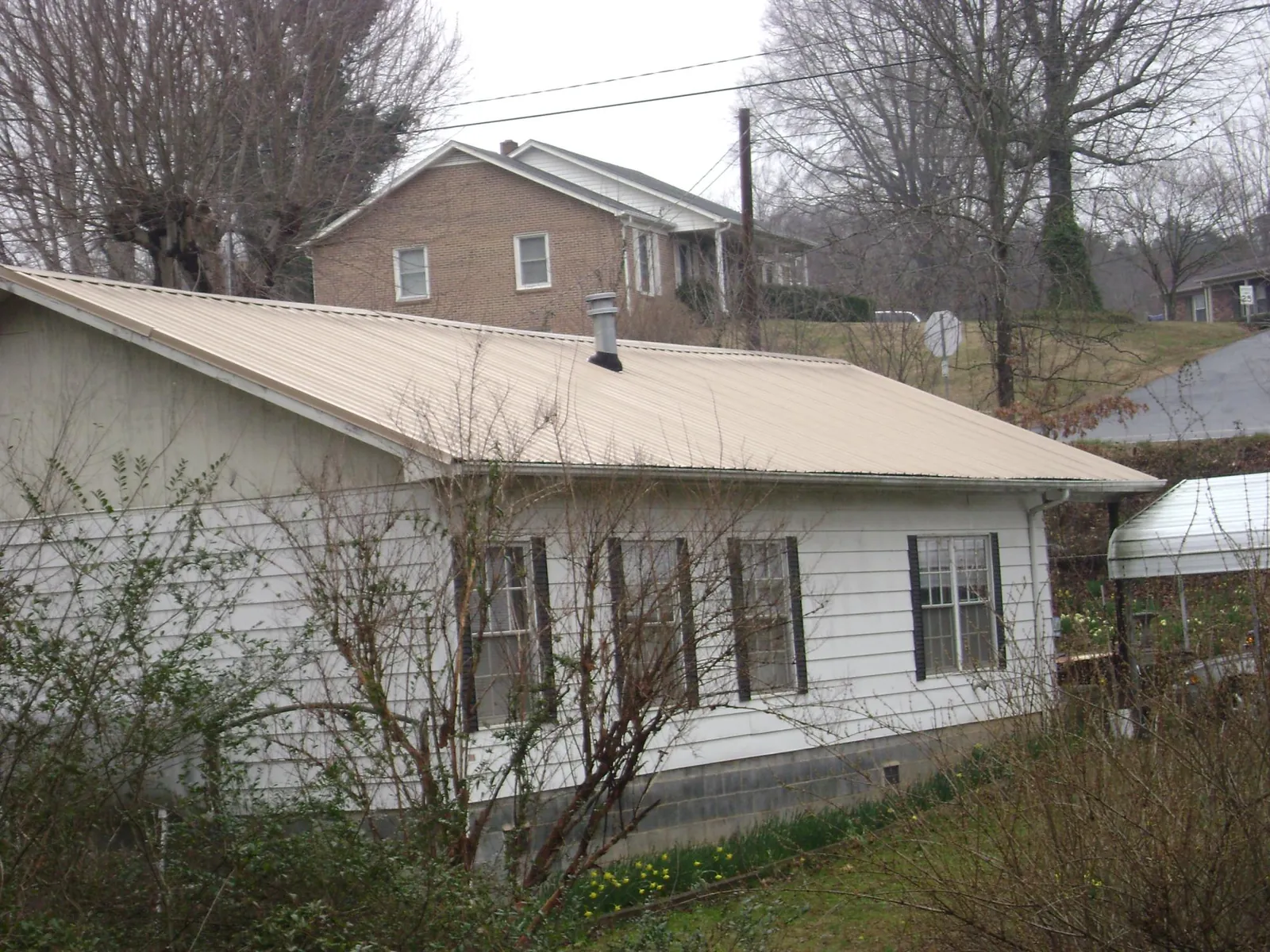 Tan metal roof on a white sided house set into a hillside — Commercial Roofing by Roofing Brothers in Wakita
