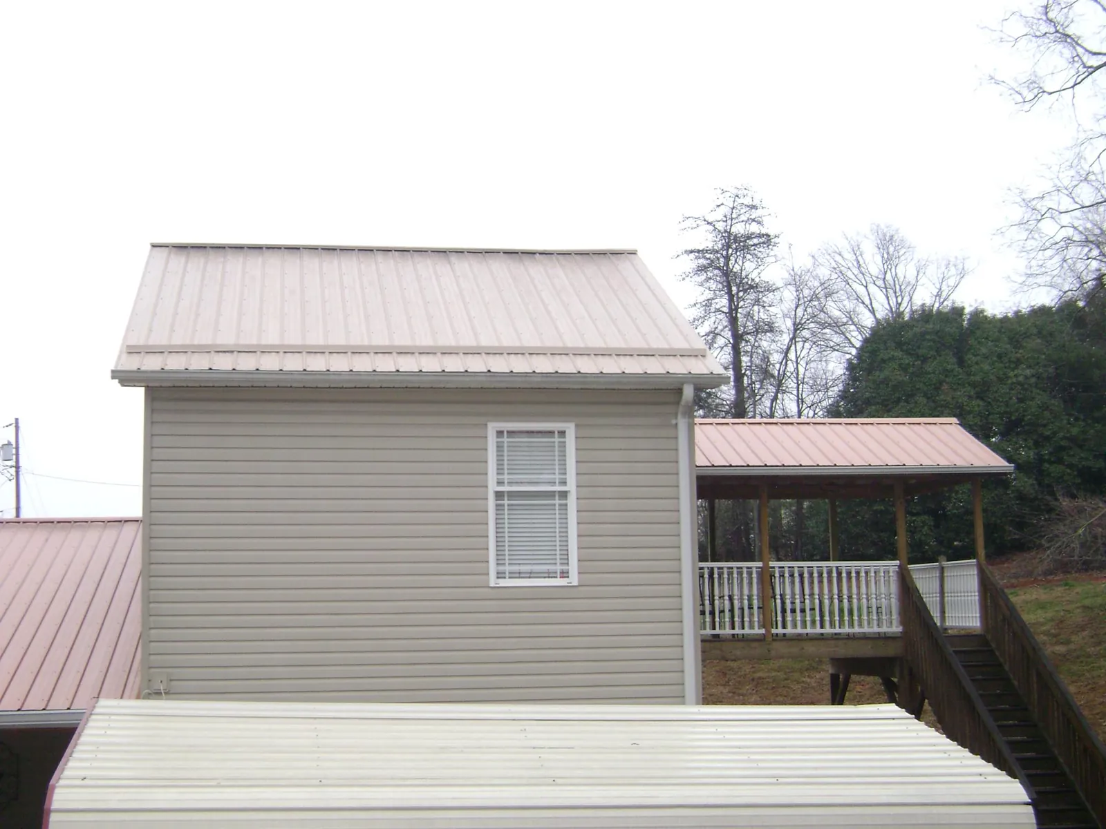 Tan metal roofs on a two story addition and attached porch, from a Roof Replacement job in Wakita